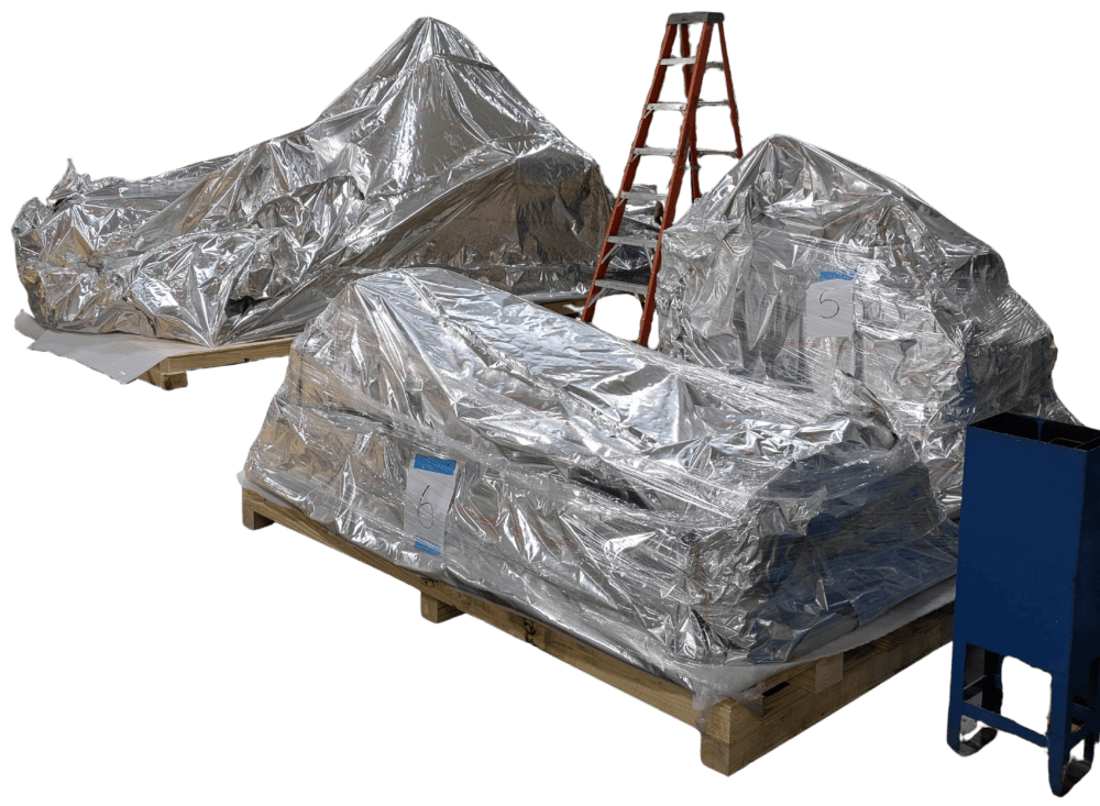 Reflective-wrapped loads on wooden pallets beside a ladder and workshop cart.